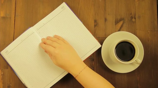 The girl writes in the diary the word love with a pink felt-tip pen and drinks coffee. Time laps