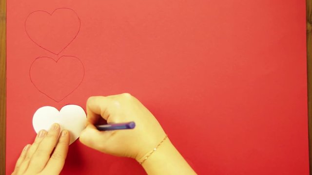 The girl draws on a red cardboard hearts. Close-up