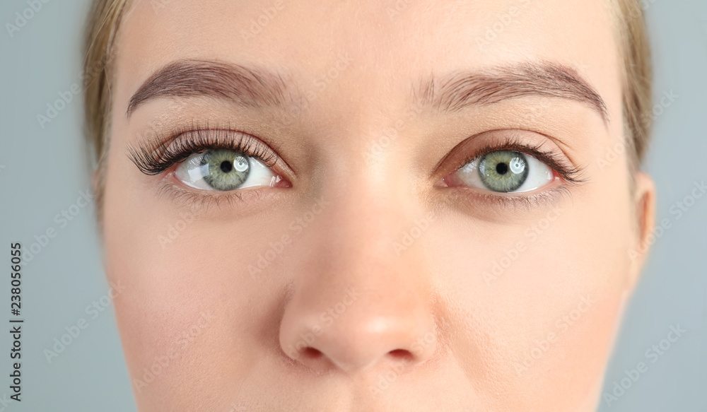 Wall mural young woman with beautiful eyelashes on gray background, closeup. before and after extension procedu