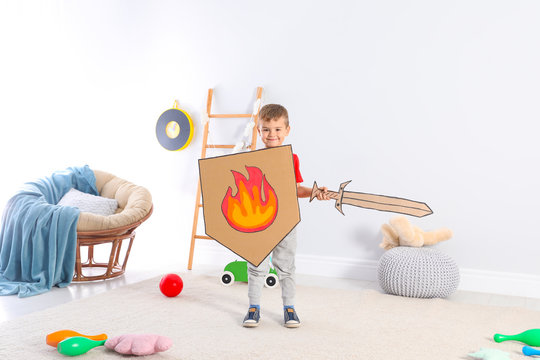 Cute little boy playing with cardboard sword and shield at home