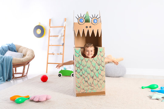 Cute little boy playing with cardboard dragon at home