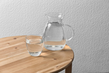 Obraz premium Pitcher and glass with water on table near white wall. Space for text