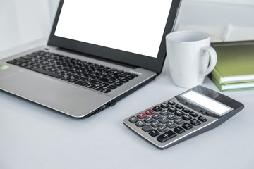 Laptop white screen ,calculator white screen ,white coffee mug and green book on the white desk