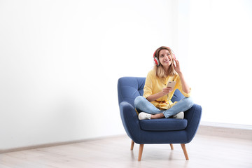 Young woman listening to music in armchair at home. Space for text
