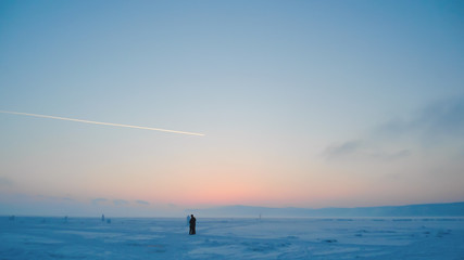 a couple in love on a romantic walk through a snowy field at sunset; winter cold; blue frosty haze over a frozen lake
