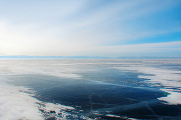 frozen lake; thick dark-blue ice; light haze in the morning; winter landscape 