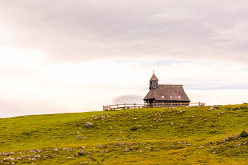 Church in the Slovenia big plateau pasture (Velika Planina). Chapel on the hill, religion symbol.Dramatic mystic clouds and colors. Green meadow and blue sky with clouds. Plateau near the Kamnik city