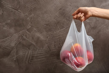 Woman holding plastic bag with apples on gray background. Closeup, space for text