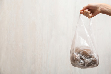 Woman holding plastic bag with potatoes on light background, closeup. Space for text
