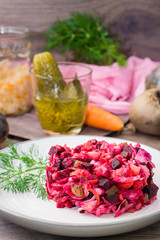 A portion of vinaigrette - a salad of boiled vegetables, sauerkraut and pickled cucumbers on a plate on a wooden table. National Russian dish