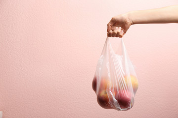 Woman holding plastic bag with apples on color background, closeup. Space for text