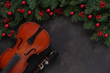Old violin and flute with fir-tree branches with Christmas decor.  Christmas and New Year's concept. Top view, close-up on dark concrete background