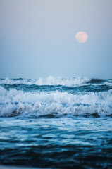 Splashing wave on the Black sea in the night with rising full moon in the background