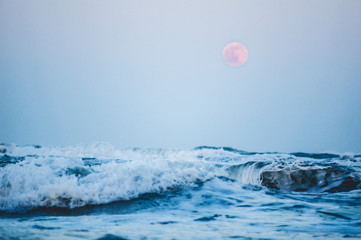 Splashing wave on the Black sea in the night with rising full moon in the background