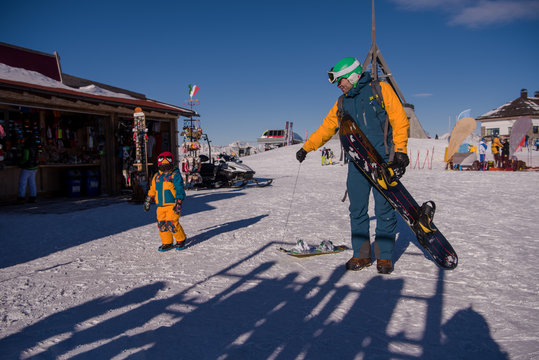 father preparing his little son for the first time on a snowboard