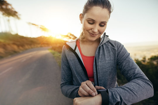 Female jogger looking at her watch walking on street