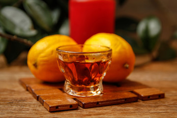 Small cup of brandy and lemon with candle. Wooden mat and wooden rustic table. Close-up.