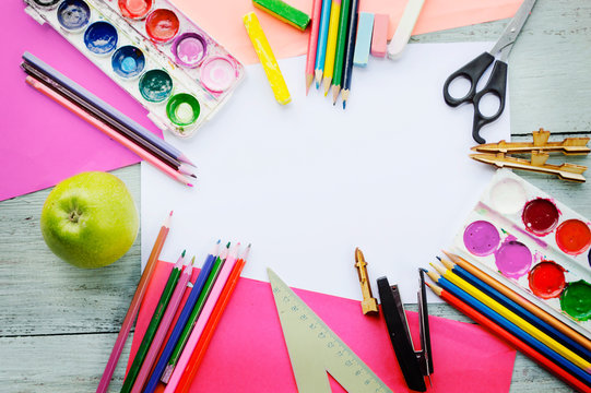 a cup with colored pencils, watercolor paints, a notebook, a ruler, a stapler, scissors on a blue wooden background, top-down view 