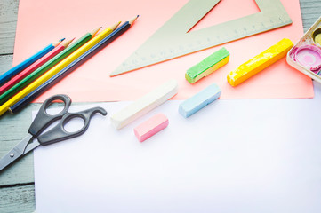 a cup with colored pencils, watercolor paints, a notebook, a ruler, a stapler, scissors on a blue wooden background, top-down view 