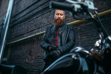 Obraz na płótnie Canvas Male biker in leather jacket puts on gloves
