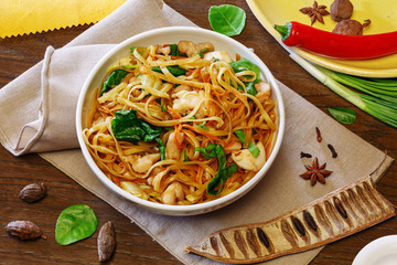 Chinese wok noodles with meat and vegetables in a plate on a wooden background