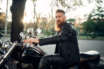 Baerded biker poses on chopper leaning on a helmet