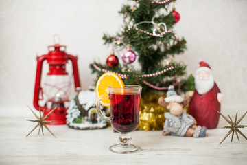 Christmas decor, tree, gold pumpkin, deer, gift, Santa, star, gingerbread house, red lantern on the wooden table. White wood background Hot mulled wine drink with orange in a glass cup Christmas eve