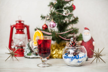 Christmas decor, tree, gold pumpkin, bump in glass vase, red lantern on the wooden table. White wood background Hot mulled wine drink with orange in a glass cup Christmas eve