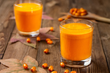 Two glasses of fresh pressed sea buckthorn juice, with autumn leaves and sea buckthorn berries and a wooden spoon on a natural blurred background.