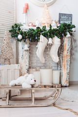 Christmas interior decorations: many balls, toys on the fireplace with big candles and woolen white socks, big clocks on the background, sled and white bear