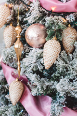 Christmas tree with beautiful winter decorations, pink ball, white cones, golden icicles, pink tape and snowflackes on the brunches. Closeup picture. Home interior. New Year holidays.
