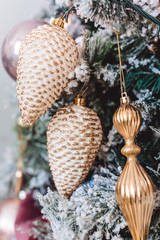 Christmas tree with beautiful winter decorations, pink ball, white cones, golden icicles, pink tape and snowflackes on the brunches. Closeup picture. Home interior. New Year holidays.