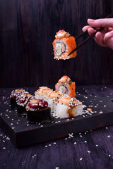 Female hand is holding a sushi roll with chopsticks