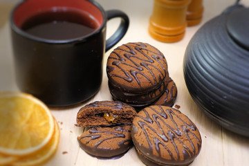 Chocolate cookies and black tea utensils. Cup and teapot. Dried orange slices. Tea scene.