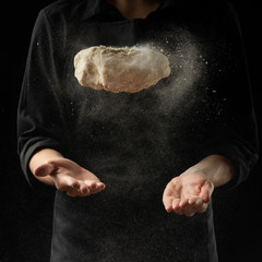 Fototapeta na wymiar Baker keeps yeast dough on a black background with frozen flour in the air, bread, brioche, croissants, pizza, pasta. Concepts of food