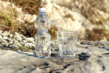 Una botella de agua mineral,con vaso sobre una roca
