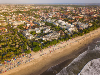 KUTA, BALI / INDONESIA - OCTOBER 25, 2018: Aerial view of Kuta town and beach with sun umbrellas lined up on the sand