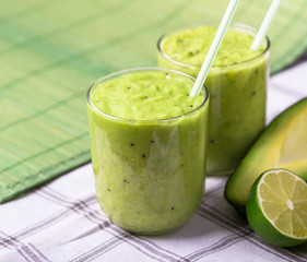 Green smoothie on green background with avocado and lemon on the right side.