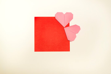 Greeting card for Valentine's Day from pink handcraft of origami hearts presented on a red frame on a white background with copy space. Top view