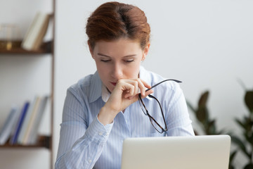 Sad worried entrepreneur working on laptop in office desk. Business woman took off her eyeglasses...