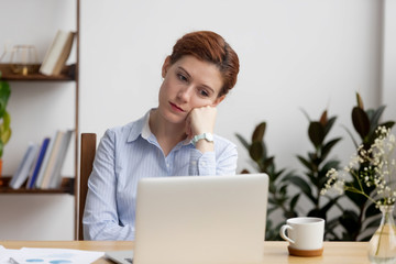 Bored female worker sitting at office desk hold head with hand has uninteresting work. Tired...