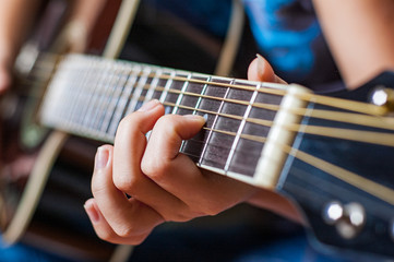 Closeup of young woman hand playing on black acoustic guitar