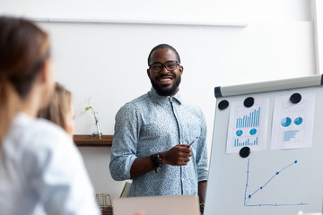 Naklejka na ściany i meble Black coach presents for company members financial report standing near whiteboard where shown sales statistics in graphs. Confident company owner teach interns acquaints with nuances of the market