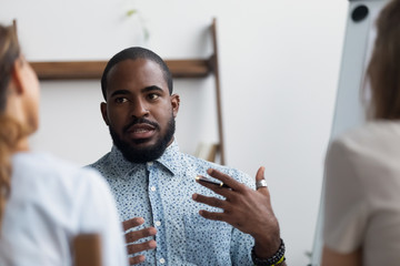 Workers brainstorming at meeting, focus on black team leader telling ideas share information or...