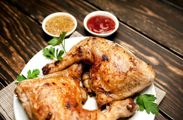 Chicken legs in a plate with mustard and ketchup on a wooden background.