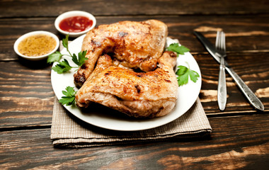 Chicken legs in a plate with mustard and ketchup on a wooden background.