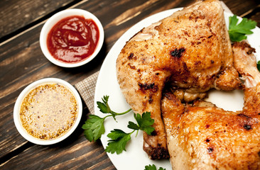 Chicken legs in a plate with mustard and ketchup on a wooden background.