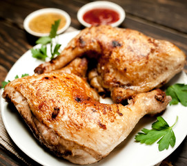 Chicken legs in a plate with mustard and ketchup on a wooden background.