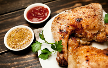 Chicken legs in a plate with mustard and ketchup on a wooden background.