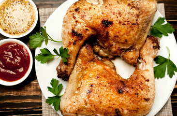 Chicken legs in a plate with mustard and ketchup on a wooden background.